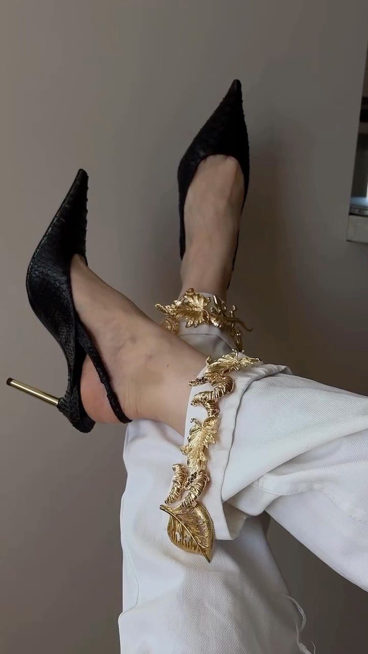 Black stiletto heels and white jeans decorated with large gold leaf appliqués.