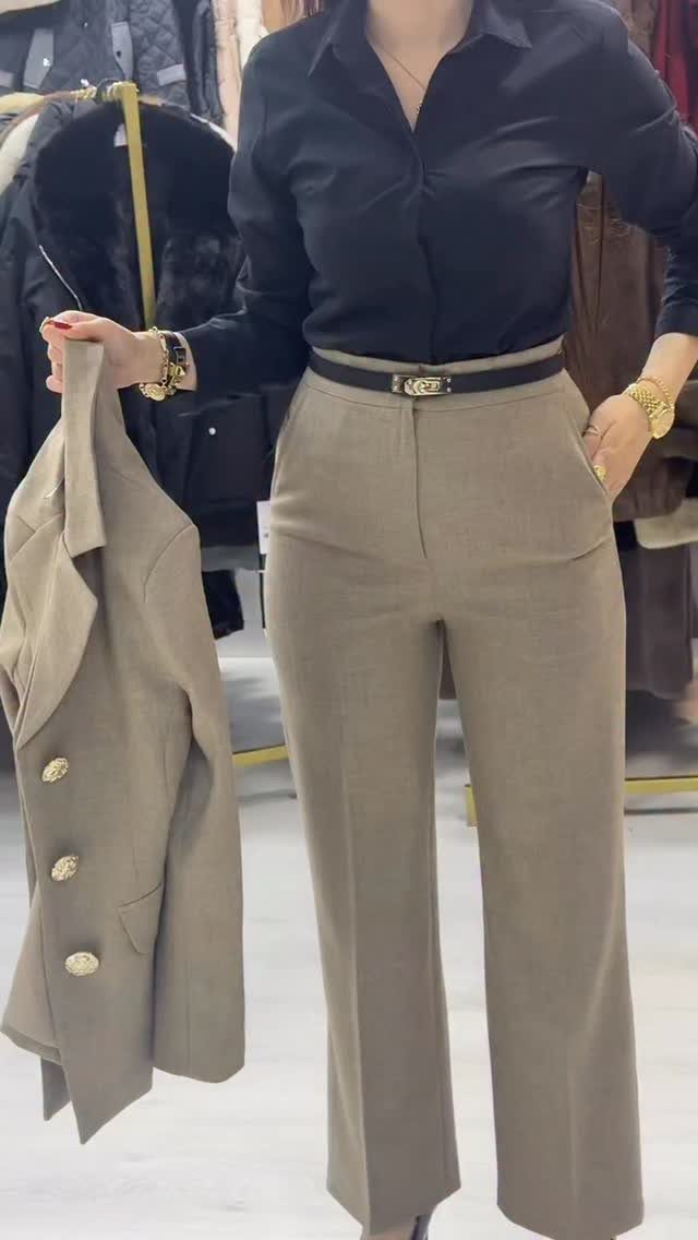Person wearing a black shirt and beige trousers holding a matching beige blazer.