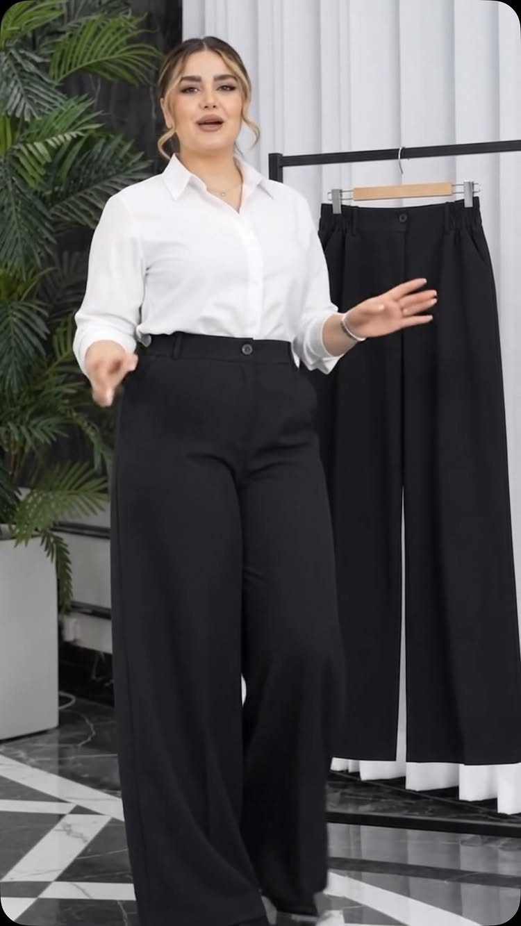 Woman wearing a white shirt and wide-leg black dress pants standing in a bright room.