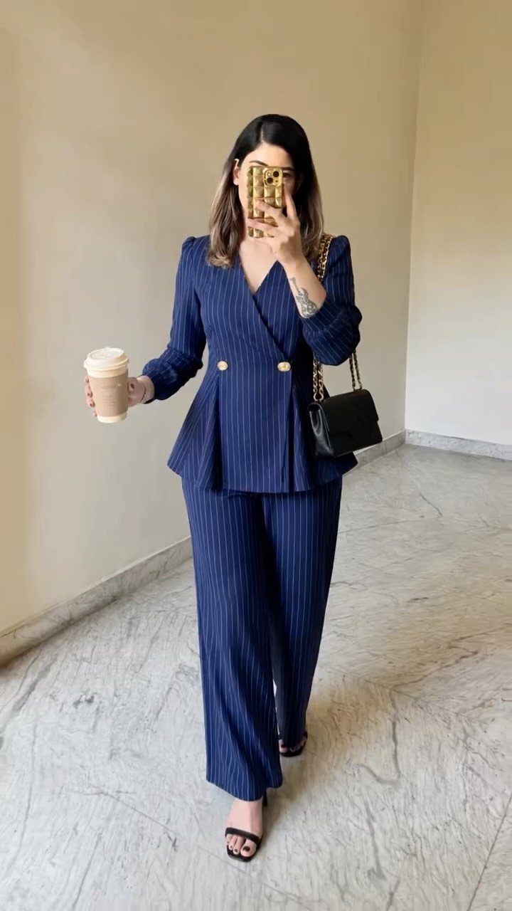 Woman in a navy pinstriped blazer and matching wide-leg trousers holding a coffee cup.