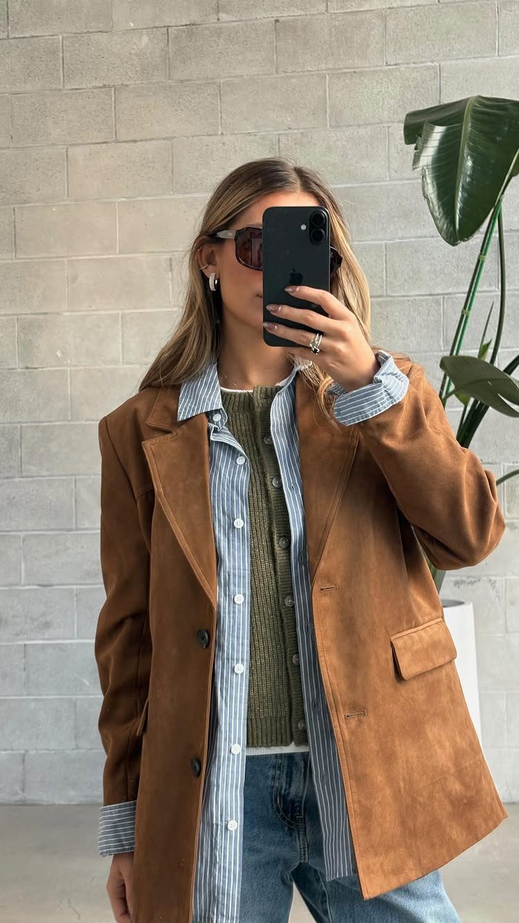 Woman wearing a brown suede blazer layered over a striped shirt and green sweater.