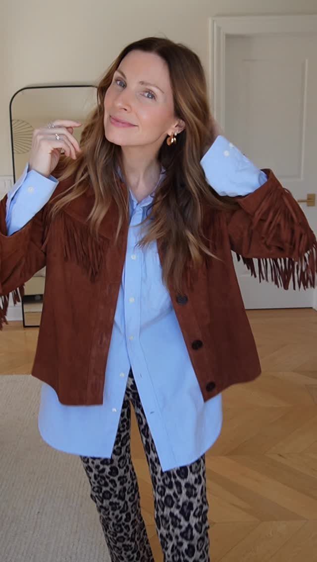 A woman wearing a fringed brown suede jacket, blue shirt, and leopard print pants.