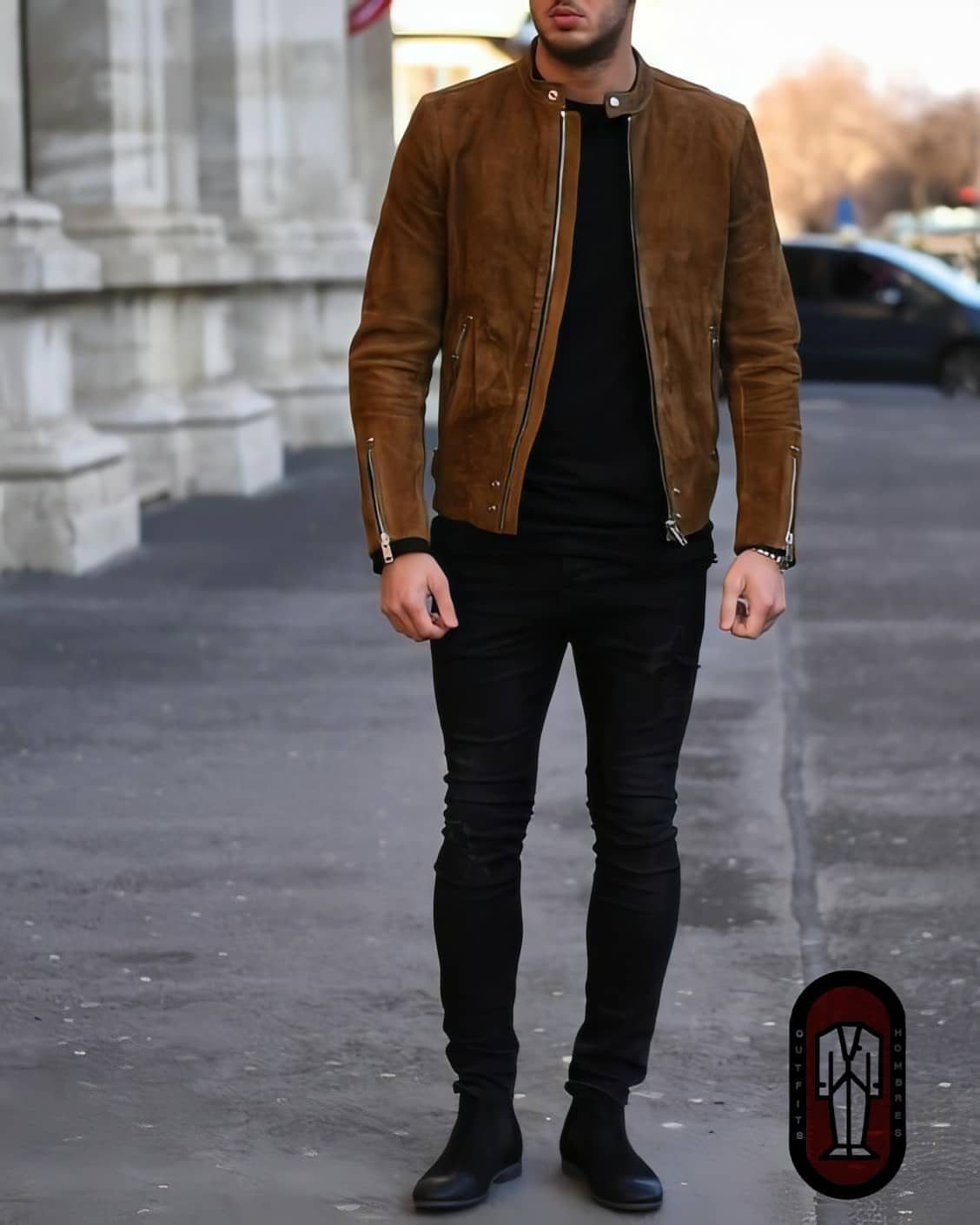 Man wearing a brown suede jacket, black t-shirt, black jeans, and black boots standing on a city street.