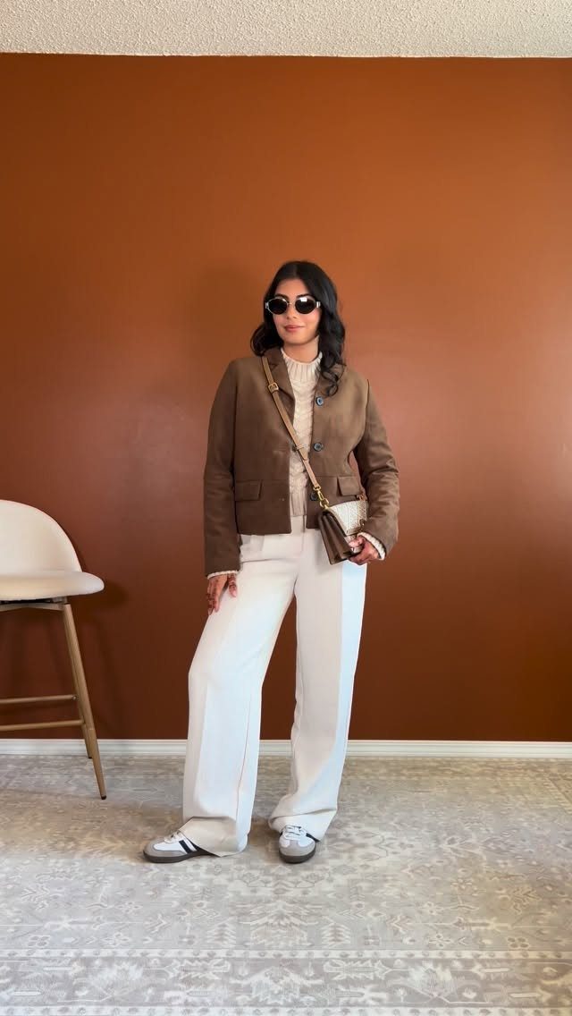 Woman wearing a brown suede jacket with cream turtleneck and white wide-leg trousers.