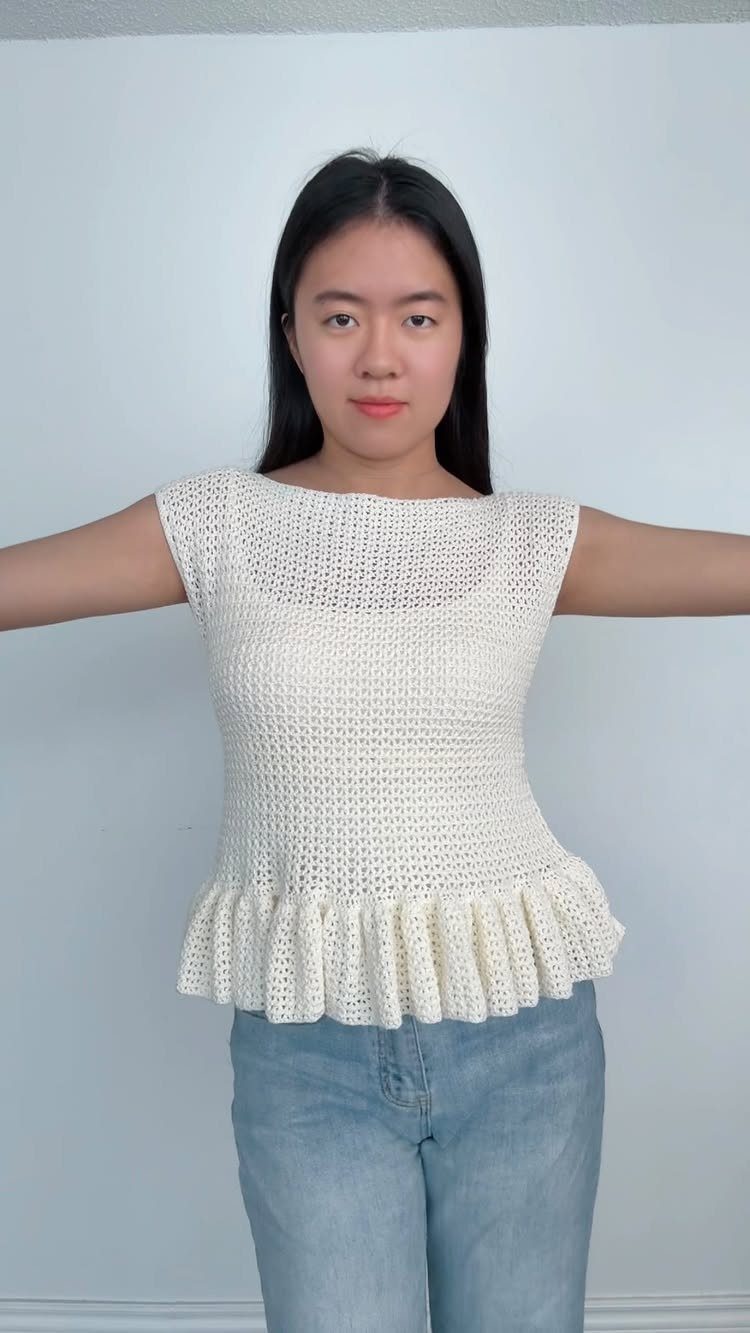 A woman wearing a white crochet top with a ruffled hem and blue denim jeans.