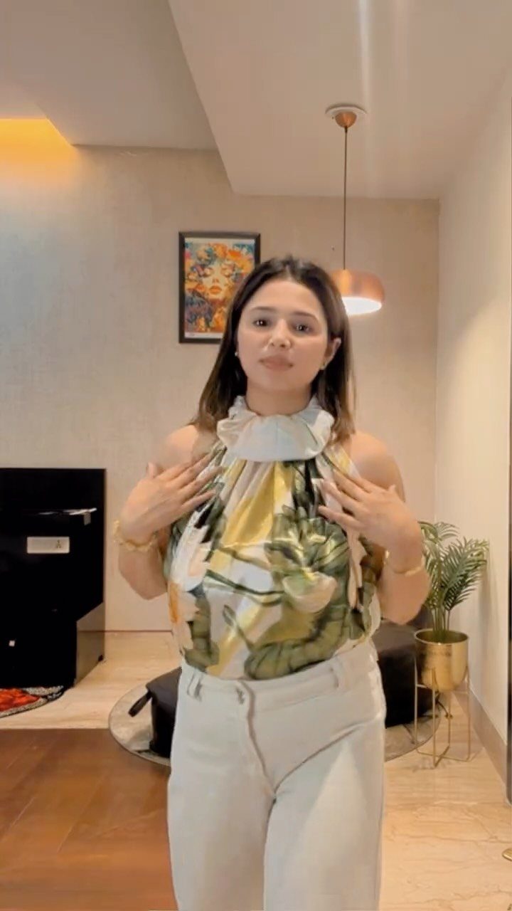Woman wearing a yellow floral patterned scarf top and white high-waisted trousers.