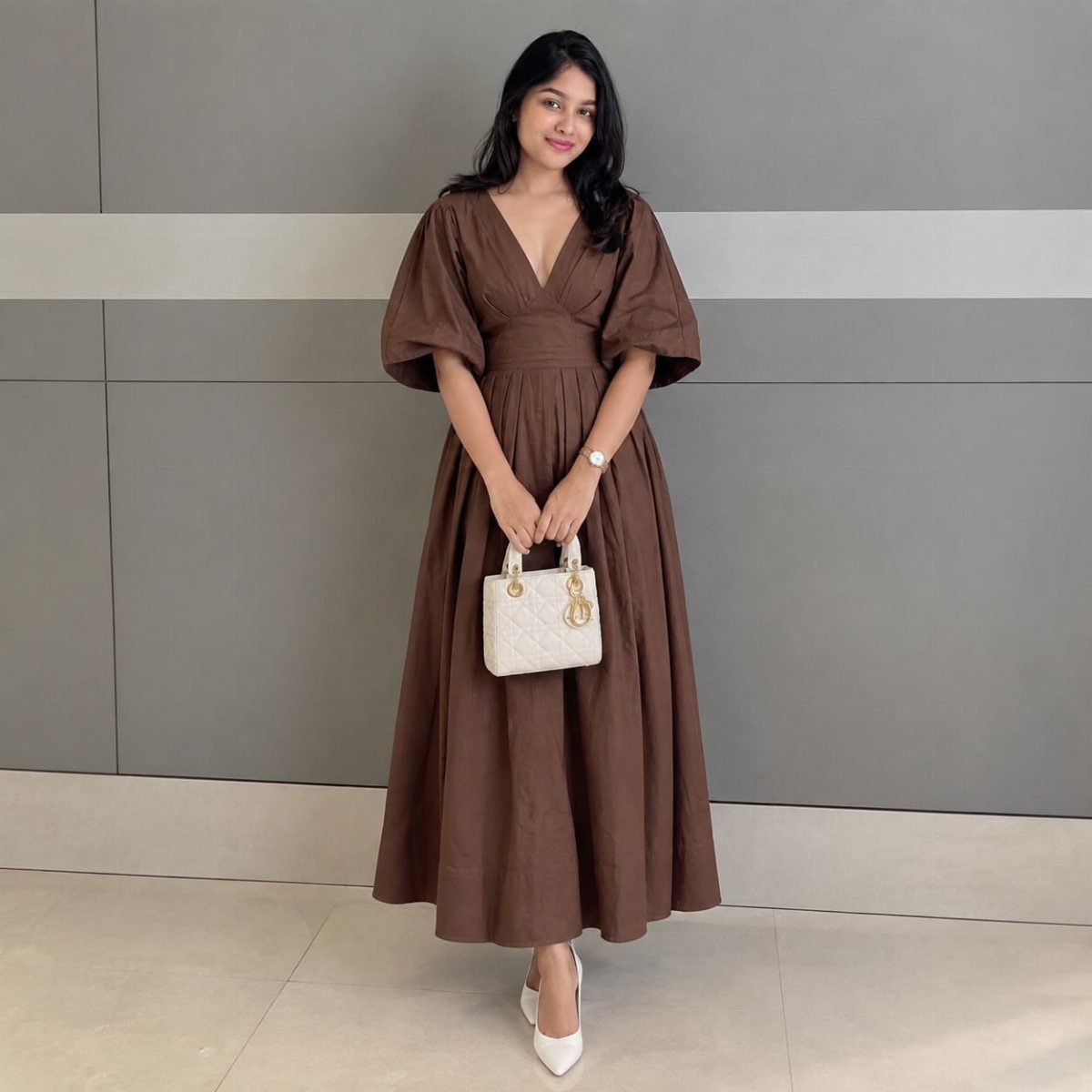 Woman posing in a brown midi dress with puff sleeves and white accessories.