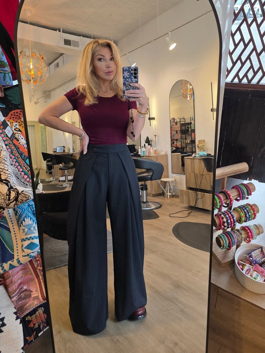 Blonde woman posing in a maroon fitted top and black wide-leg trousers.