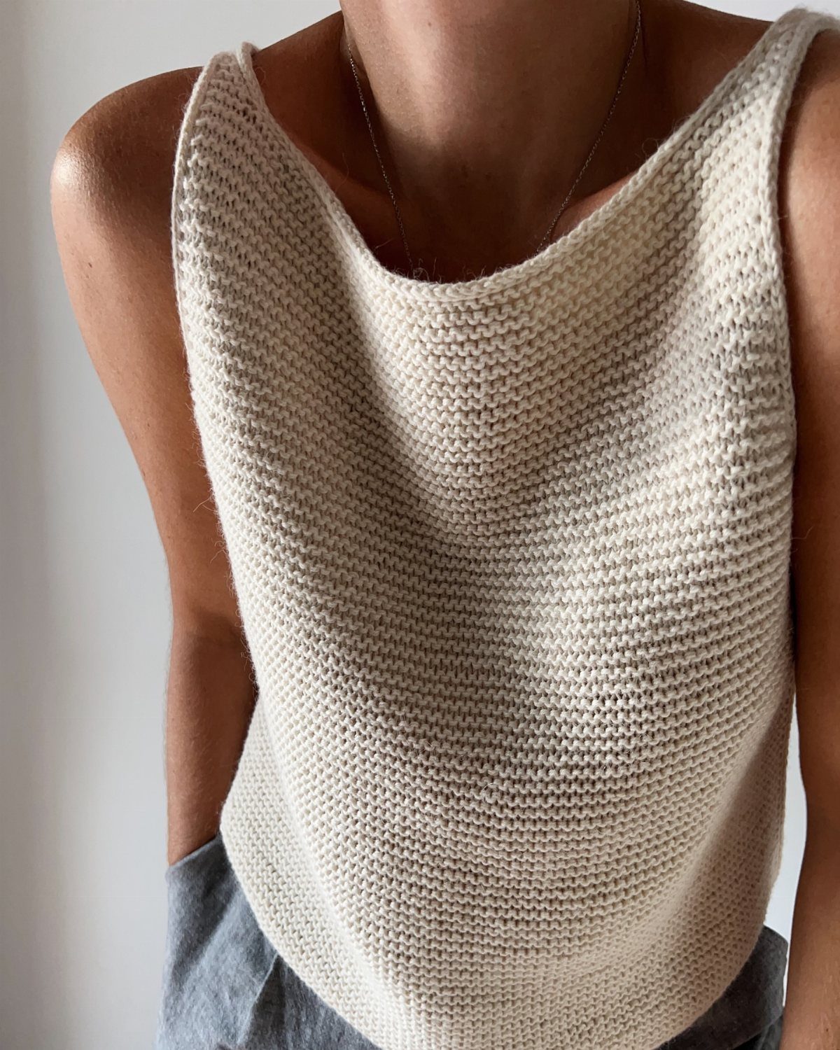 A person wearing a simple, cream-colored sleeveless knit tank top with a scoop neckline.