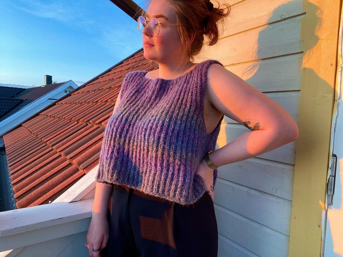 A woman wearing a purple textured sleeveless cropped knit top standing outdoors.