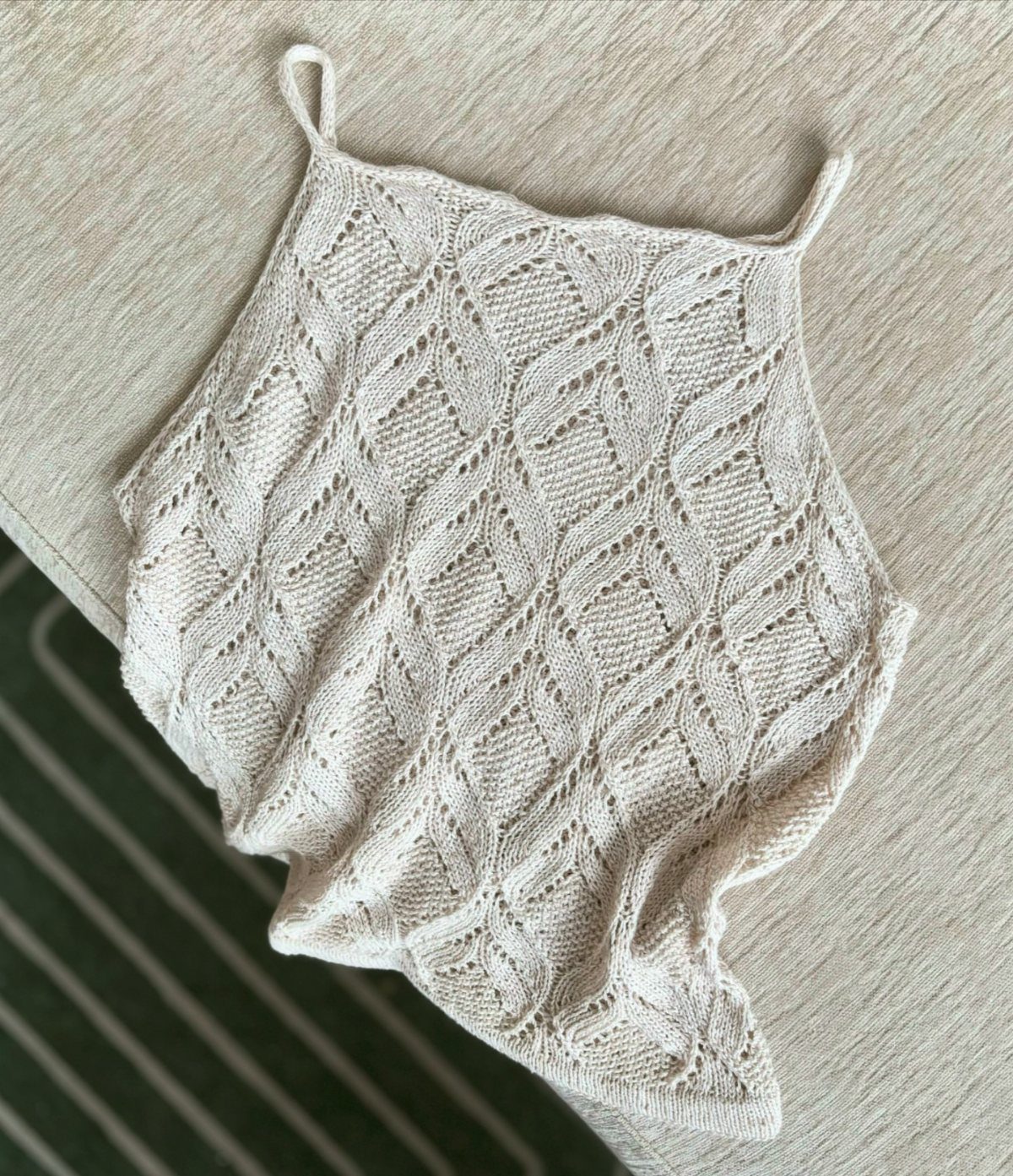 Cream knit tank top with a delicate leaf pattern lying on a textured surface.