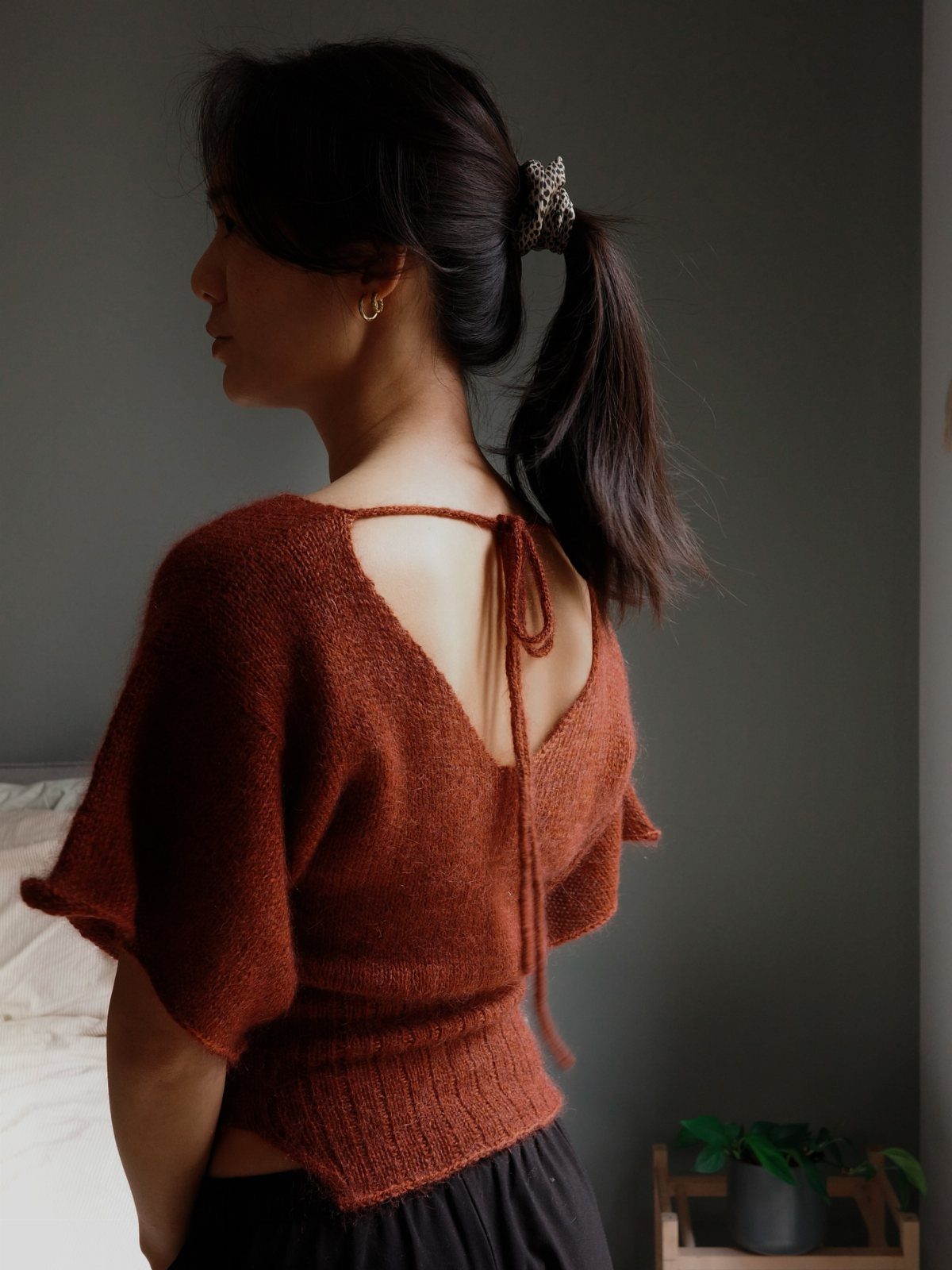 Woman wearing a rust-colored short-sleeved knit top with an open back and tie detail.