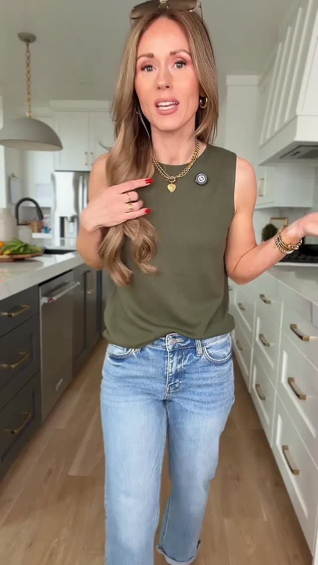 Woman wearing an olive green ribbed sleeveless tank top and light blue jeans in a kitchen.
