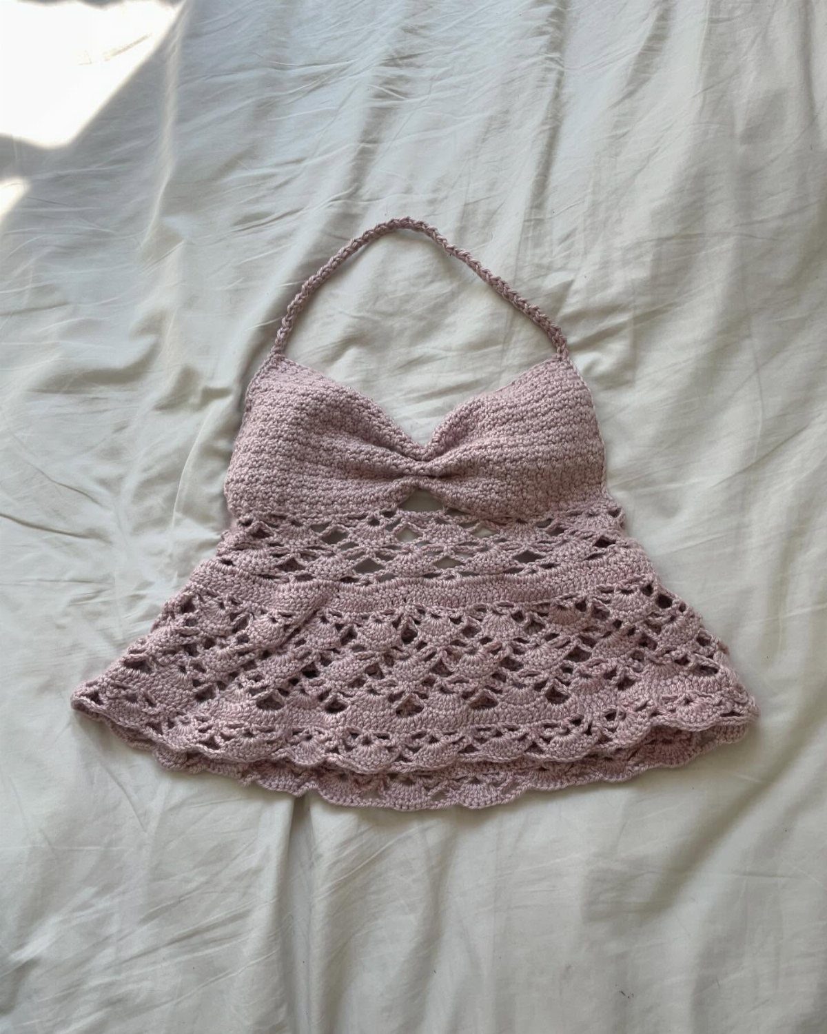 A dusty rose pink crochet halter top with a flared tiered bottom on white fabric.