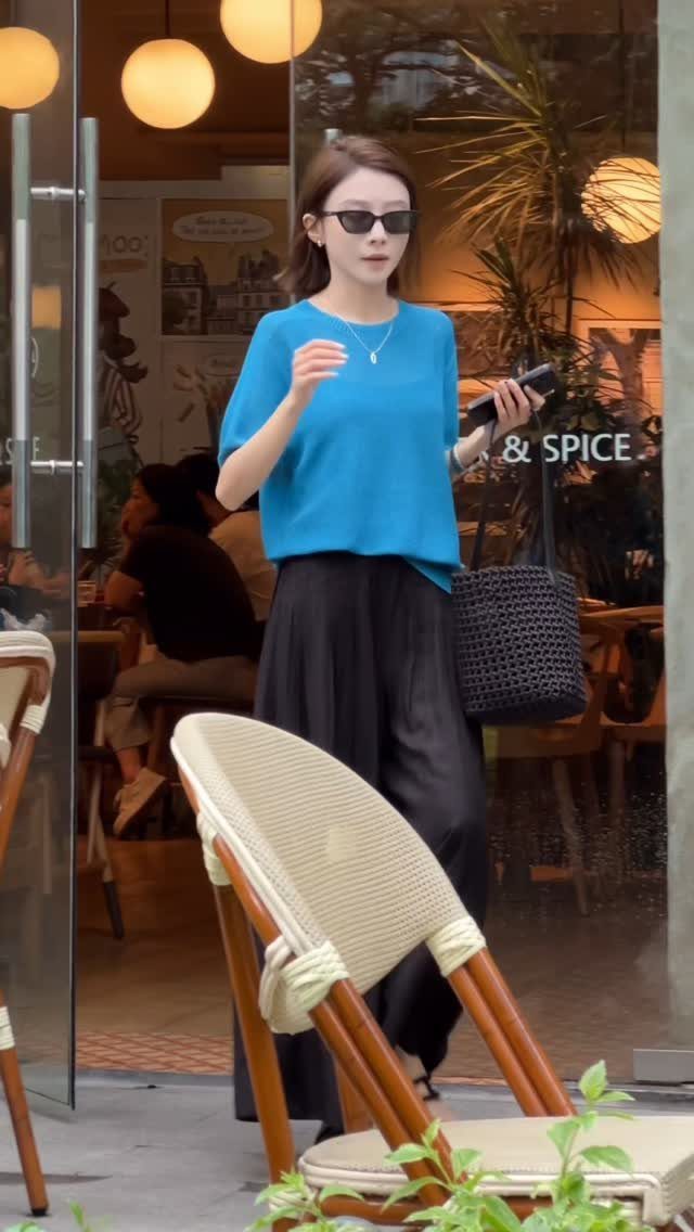 A woman in a bright blue short-sleeved knit top and long black skirt walking outdoors.