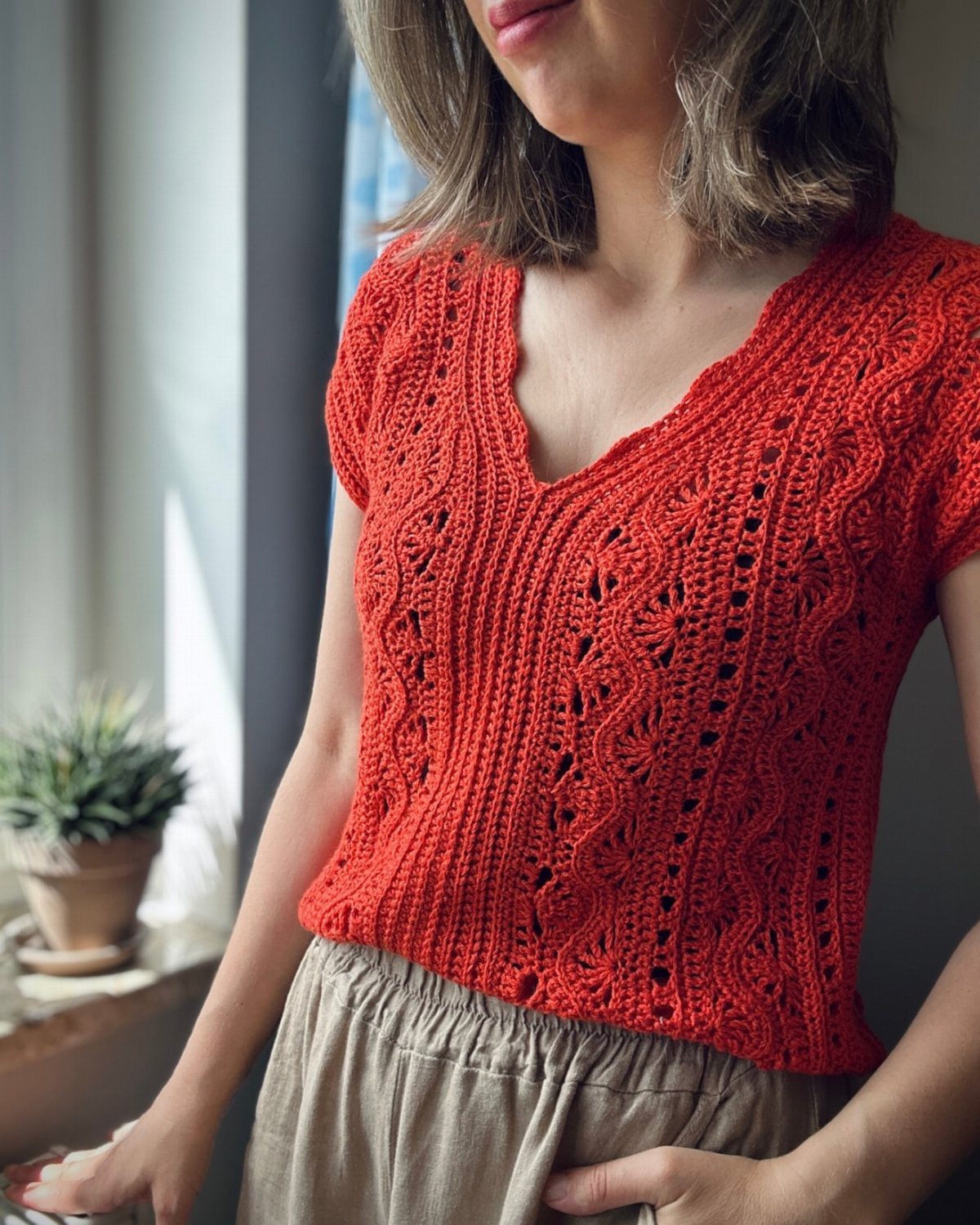 A woman wearing a bright red crochet top with intricate eyelet patterns and a V-neckline.