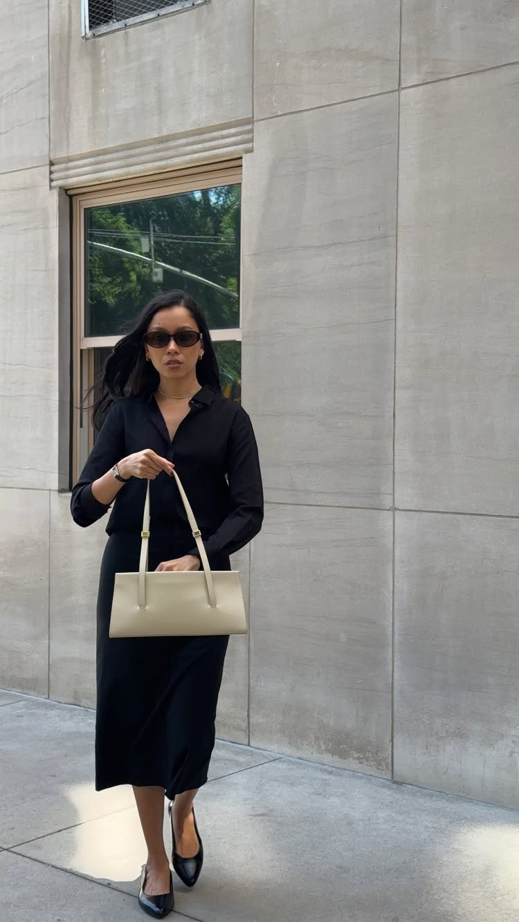 Woman in a black shirt and skirt walking with a cream tote bag.