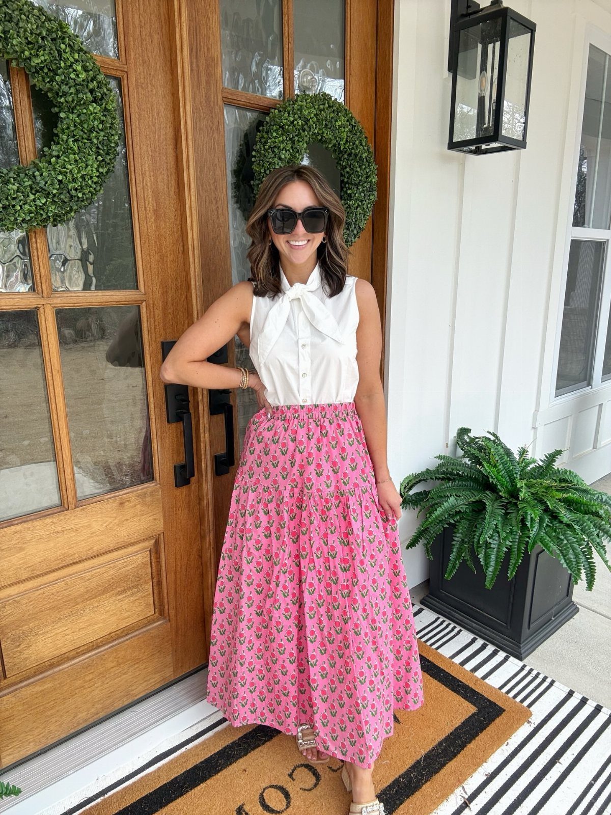 A woman wearing a white tie-neck blouse and a pink floral printed maxi skirt.