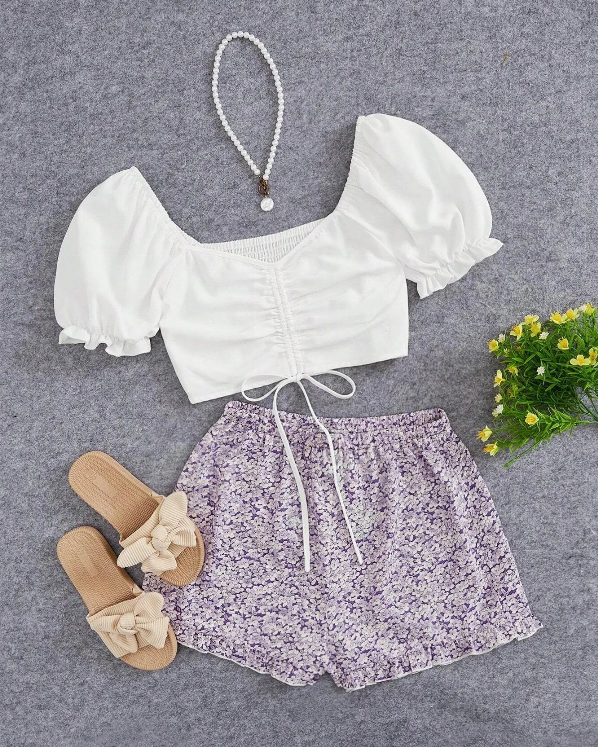 White puff-sleeve blouse and purple floral printed shorts with sandals and a pearl necklace.