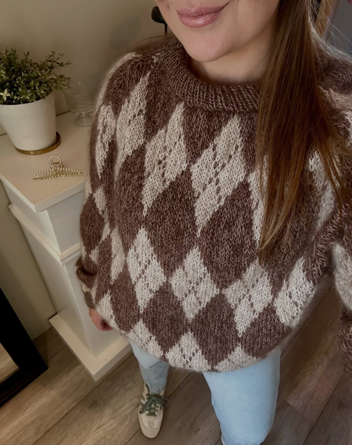 Person wearing a brown and cream argyle pattern knit sweater with light blue jeans.