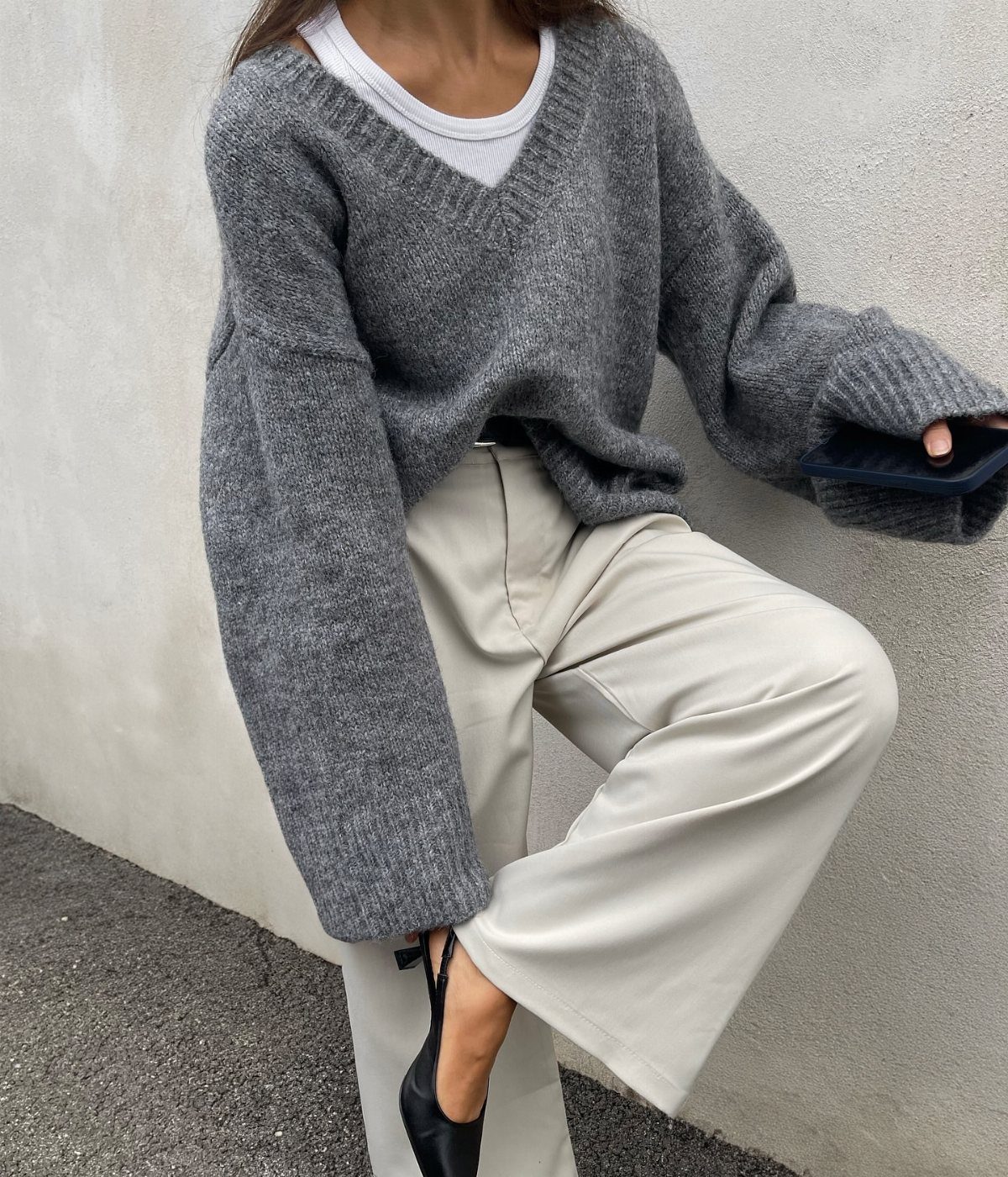 A person wearing an oversized heathered grey V-neck sweater and cream wide-leg trousers.