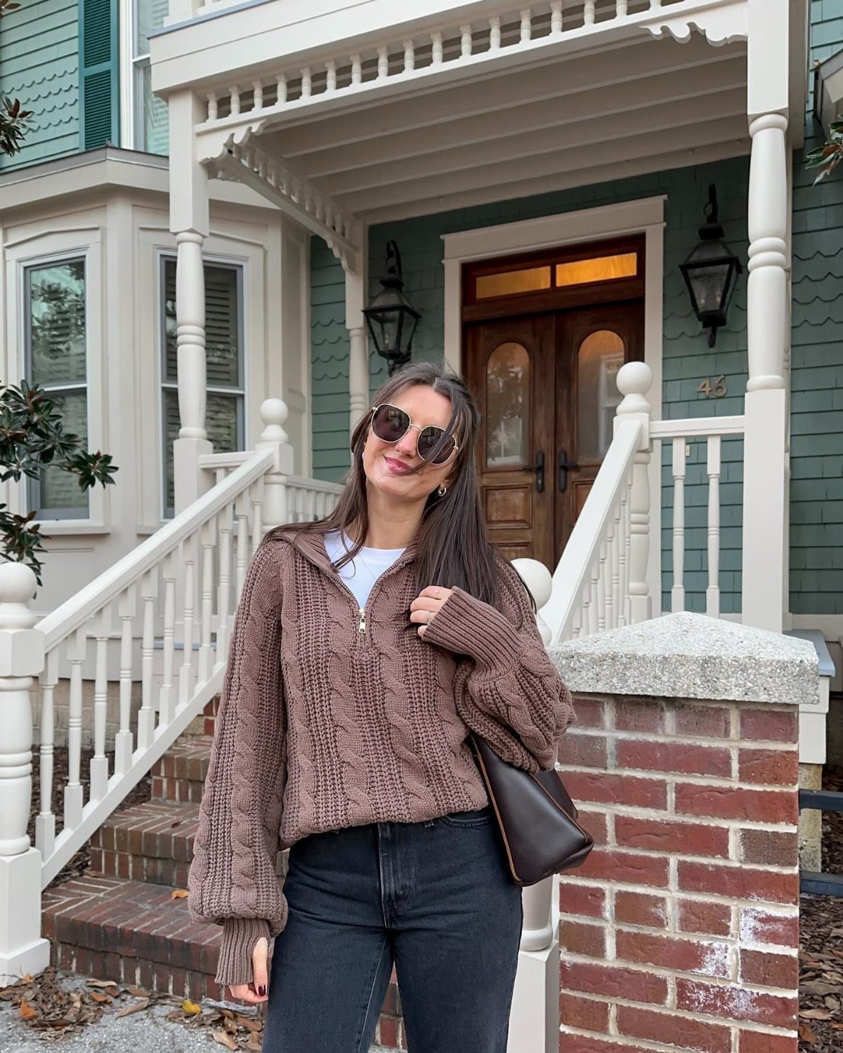 Woman wearing a brown cable knit quarter-zip sweater and dark jeans standing outdoors.