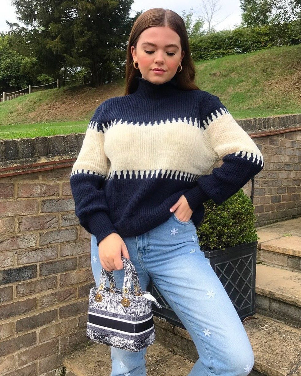 A woman posing in a navy and cream striped turtleneck sweater and star-patterned jeans.