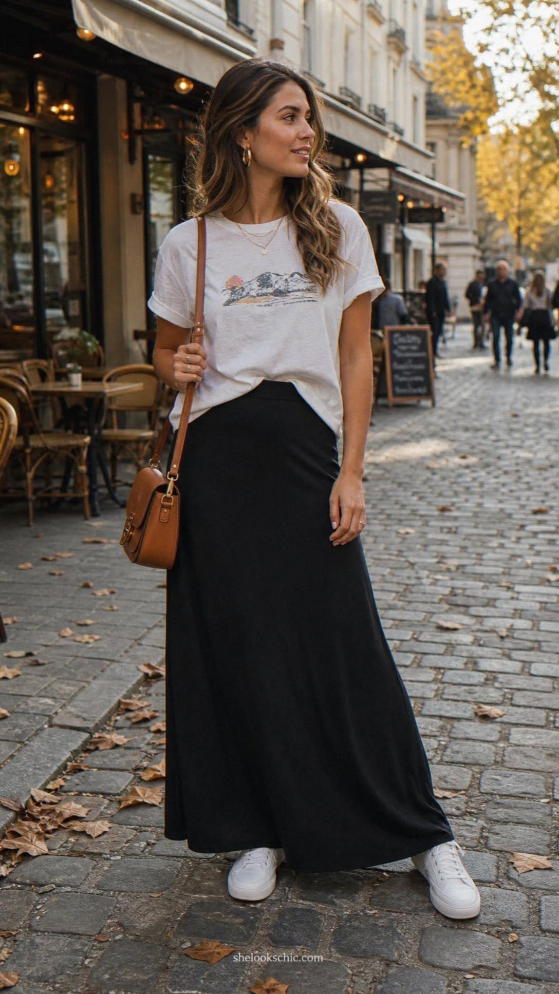 Woman wearing a white graphic t-shirt and a long black maxi skirt on a cobblestone street.