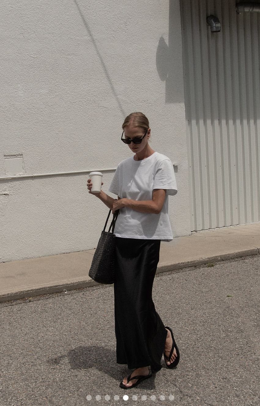 Woman walking in a white boxy t-shirt and a long black satin column skirt.