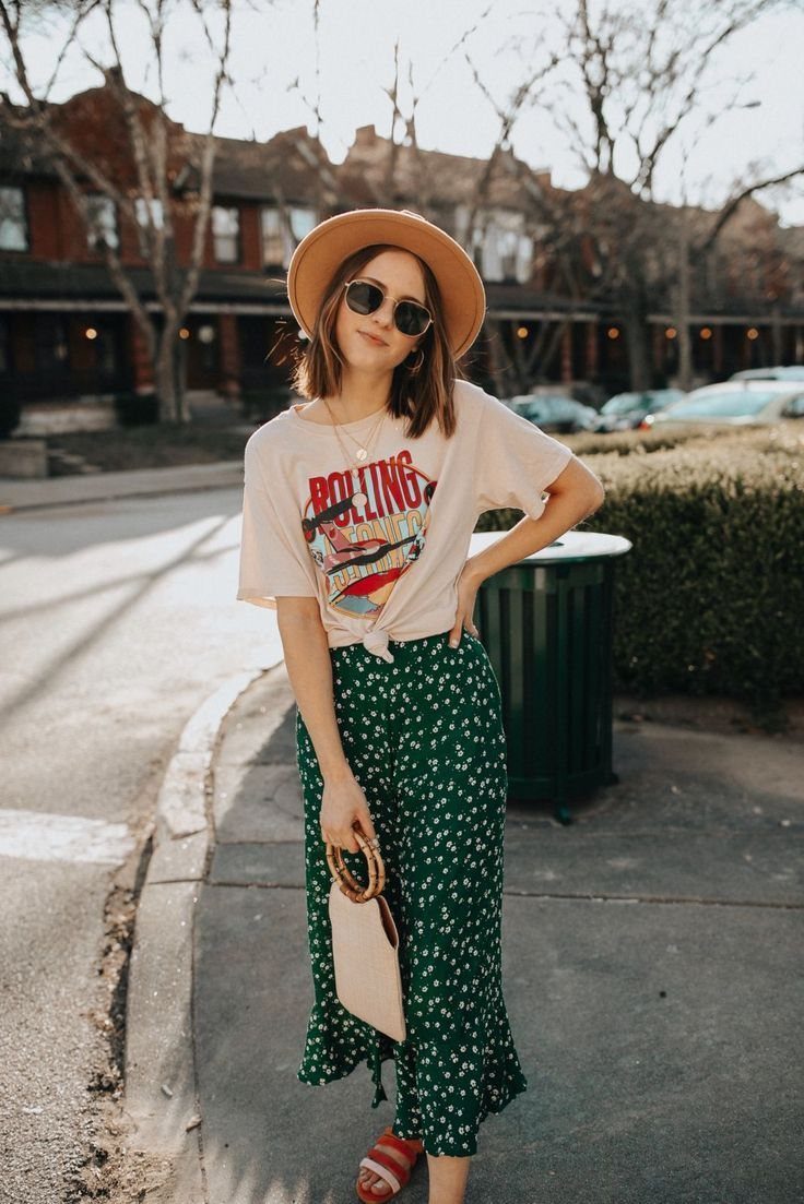 Woman in a graphic t-shirt and green floral midi skirt standing on a sidewalk.