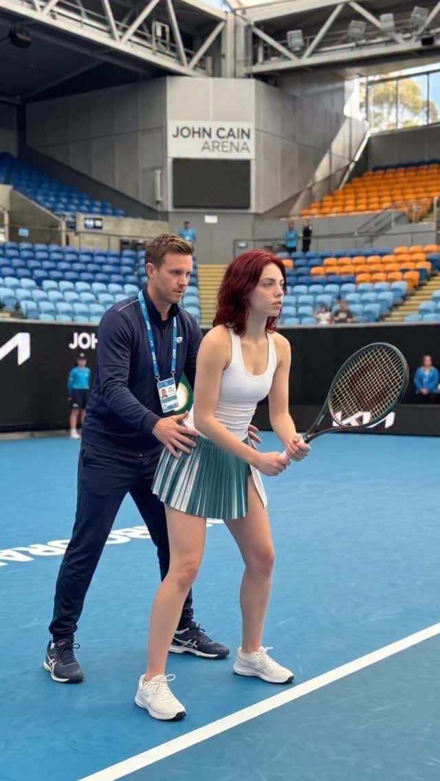 A woman in a white tank top and pleated tennis skirt holding a racket on a blue court.