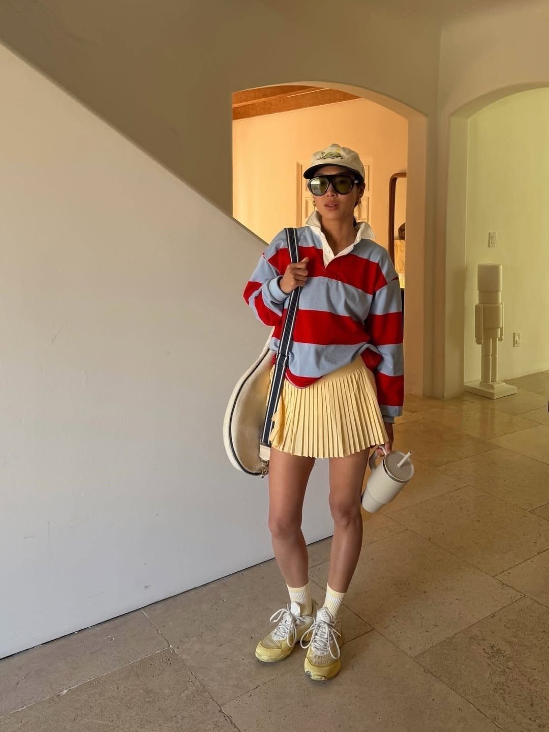 Woman in a striped polo and yellow pleated tennis skirt posing in a hallway.