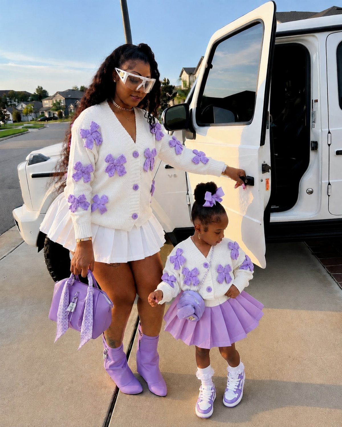 A woman and a toddler girl wearing matching white and purple coordinated outfits by a white car.