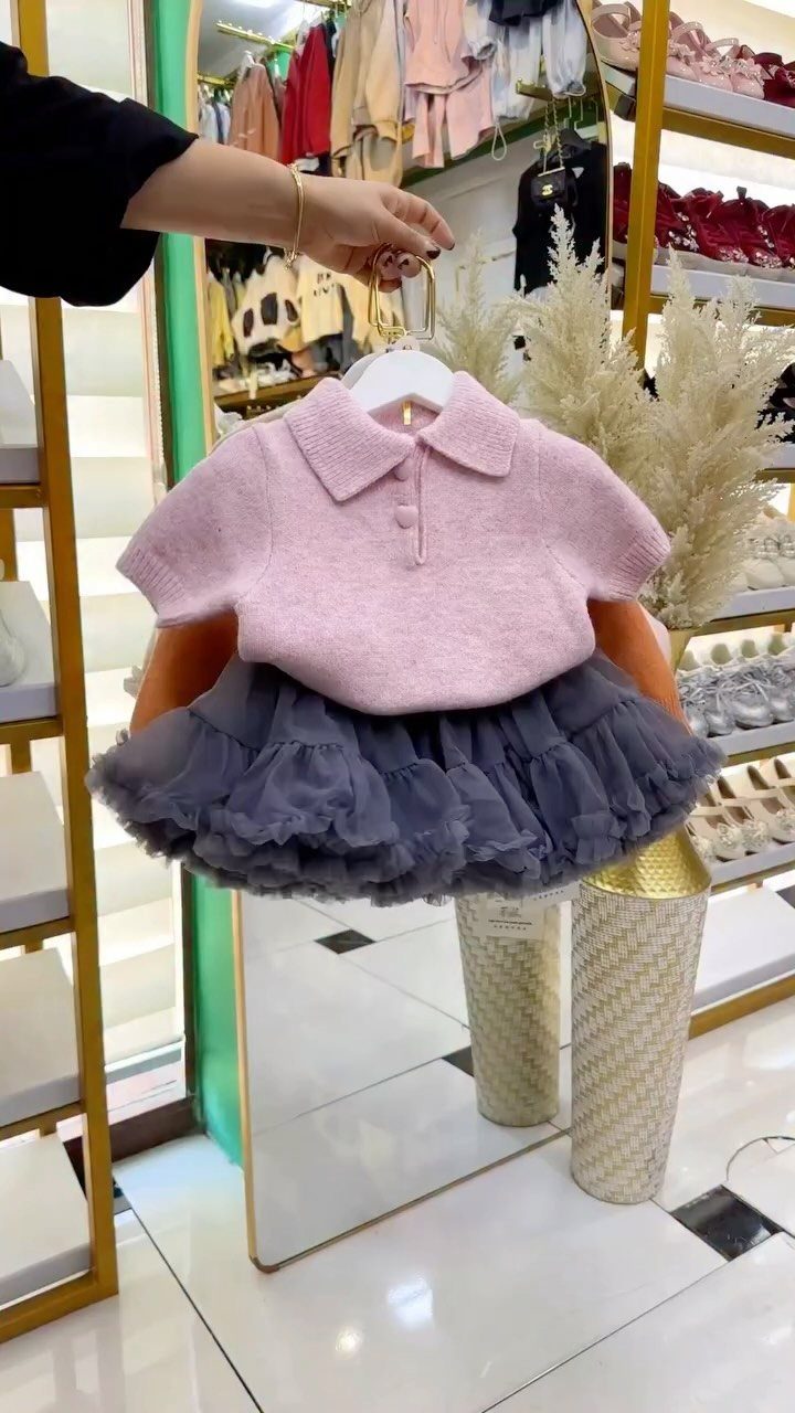 A pink polo sweater and grey tulle skirt outfit hanging on a white hanger.