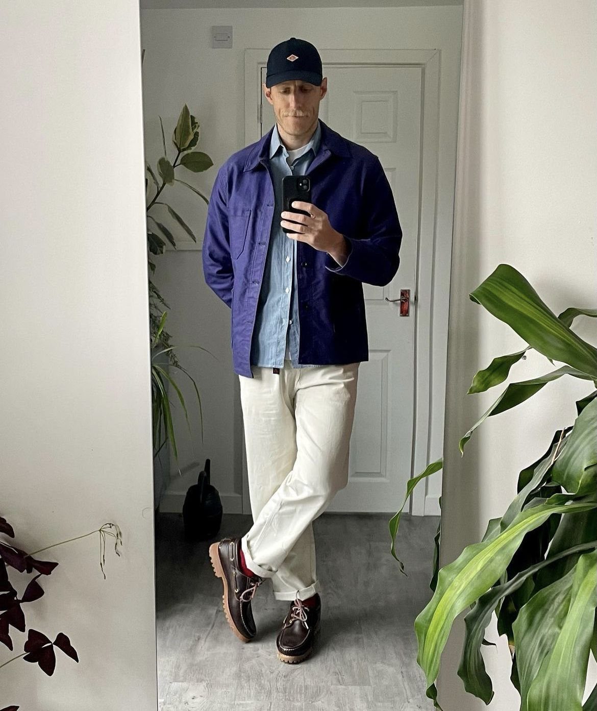 A man posing in a mirror wearing a blue jacket, white pants, and brown boat shoes.