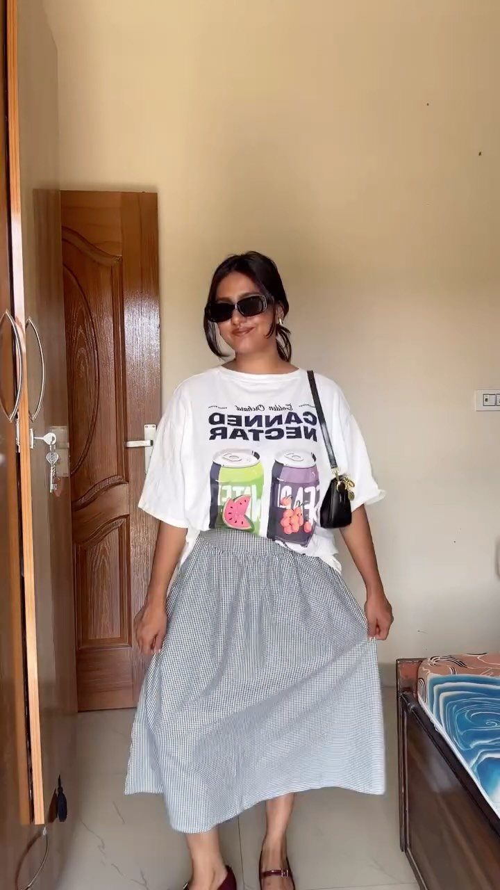 Woman wearing a white graphic t-shirt and a striped midi skirt standing indoors.