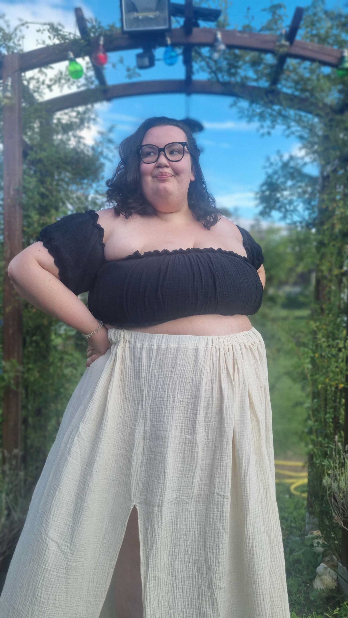 Woman in a black puff-sleeve crop top and cream midi skirt standing in a garden.