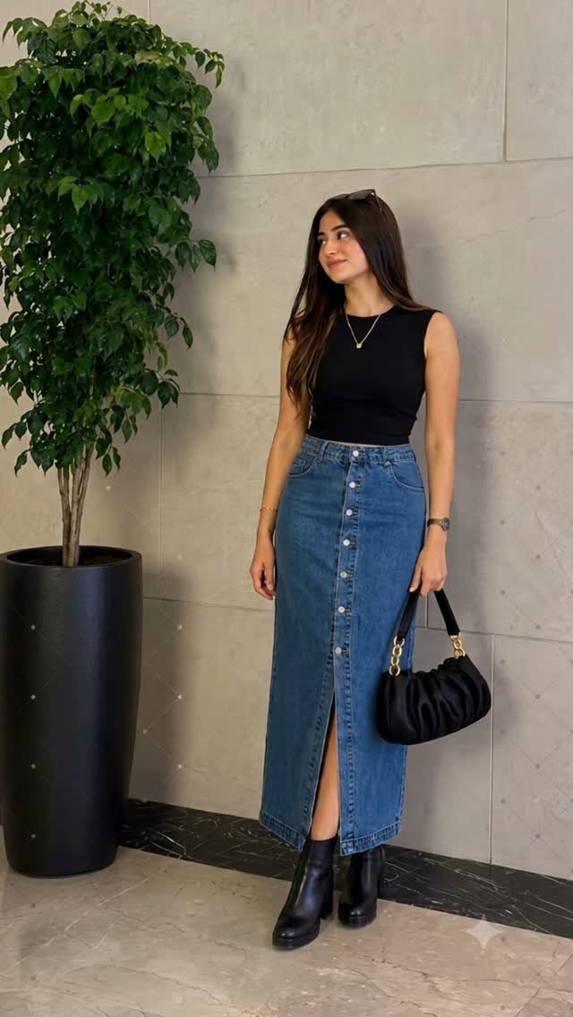 Woman wearing a black sleeveless fitted top and a long denim midi skirt with buttons.