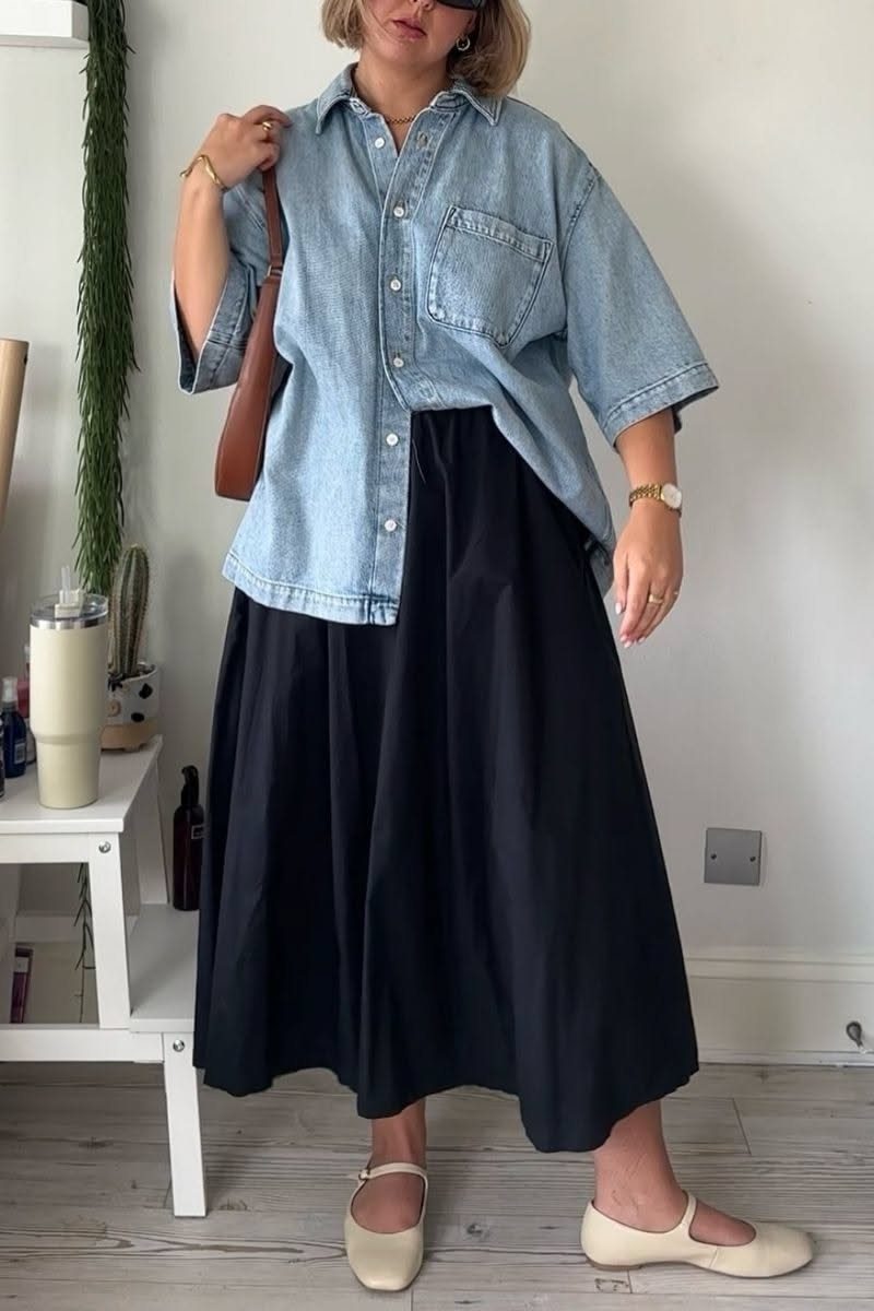 Woman wearing an oversized light blue denim shirt paired with a long black midi skirt.