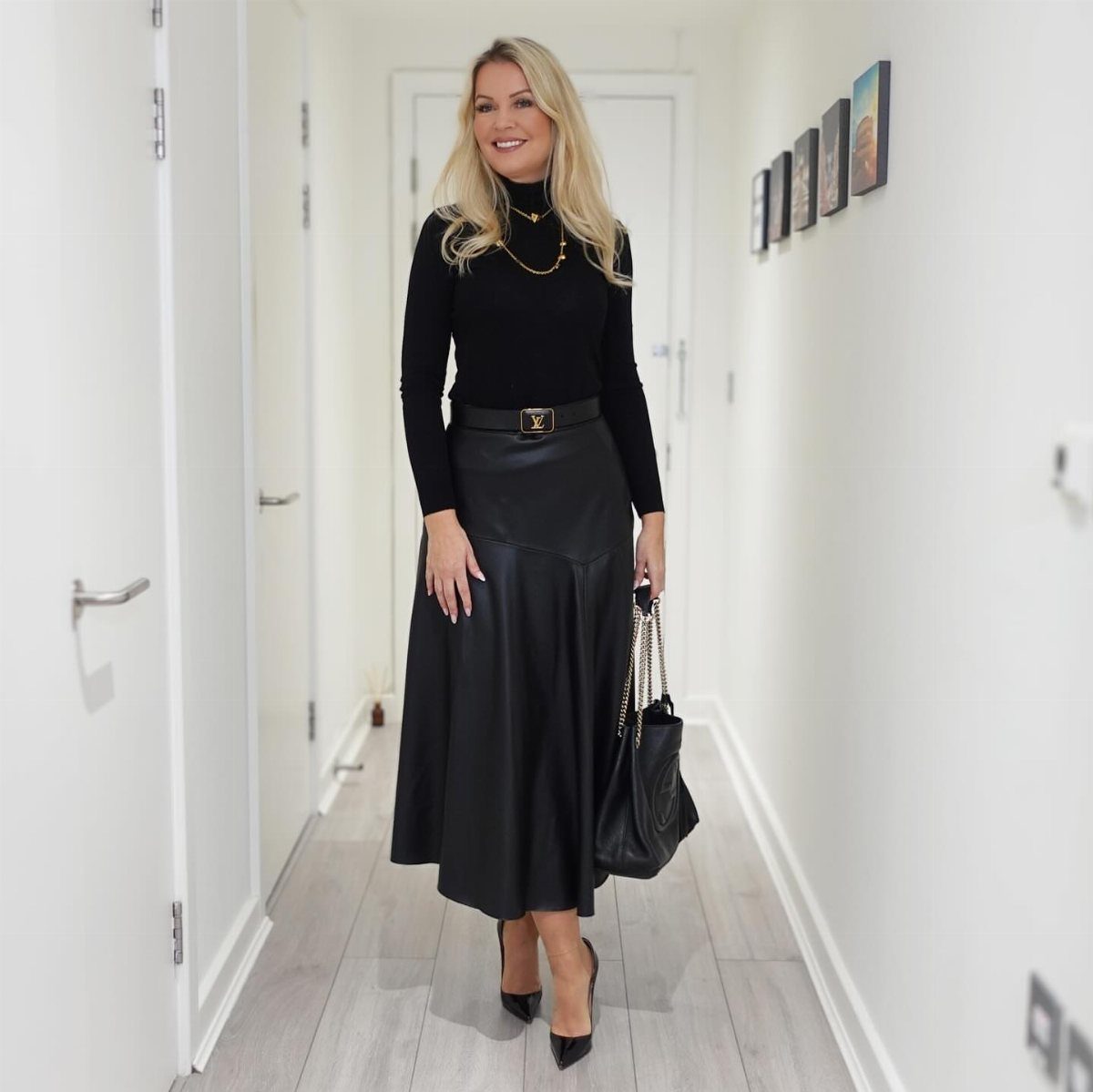 Blonde woman posing in a black thin-knit turtleneck and a black leather midi skirt.