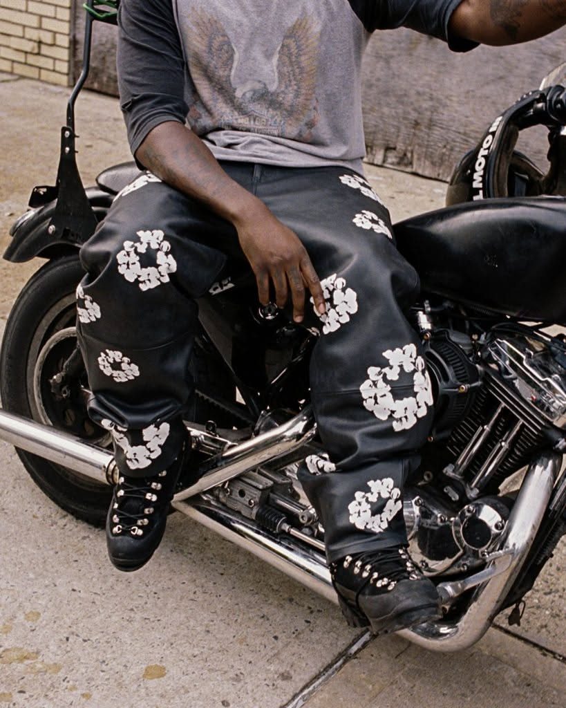 Person sitting on a black motorcycle wearing black pants with white wreath patterns.