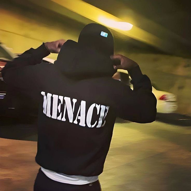 Person wearing a black Menace brand hoodie in a dark parking garage.