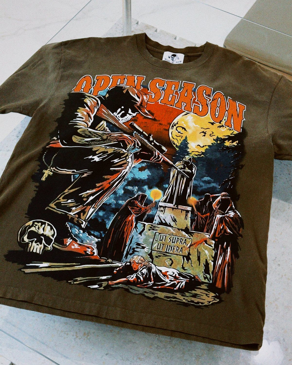 Olive green graphic t-shirt featuring a dark, cinematic illustration with a moon and hooded figures.