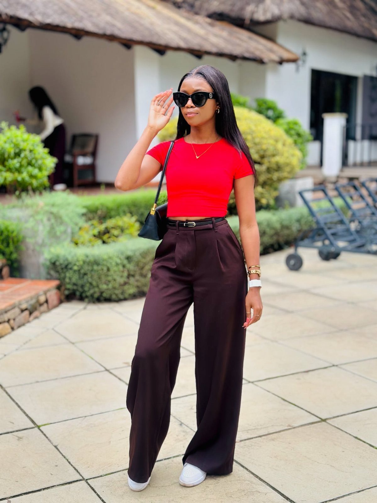 Woman in a red crop top and wide-leg dark trousers posing outdoors.