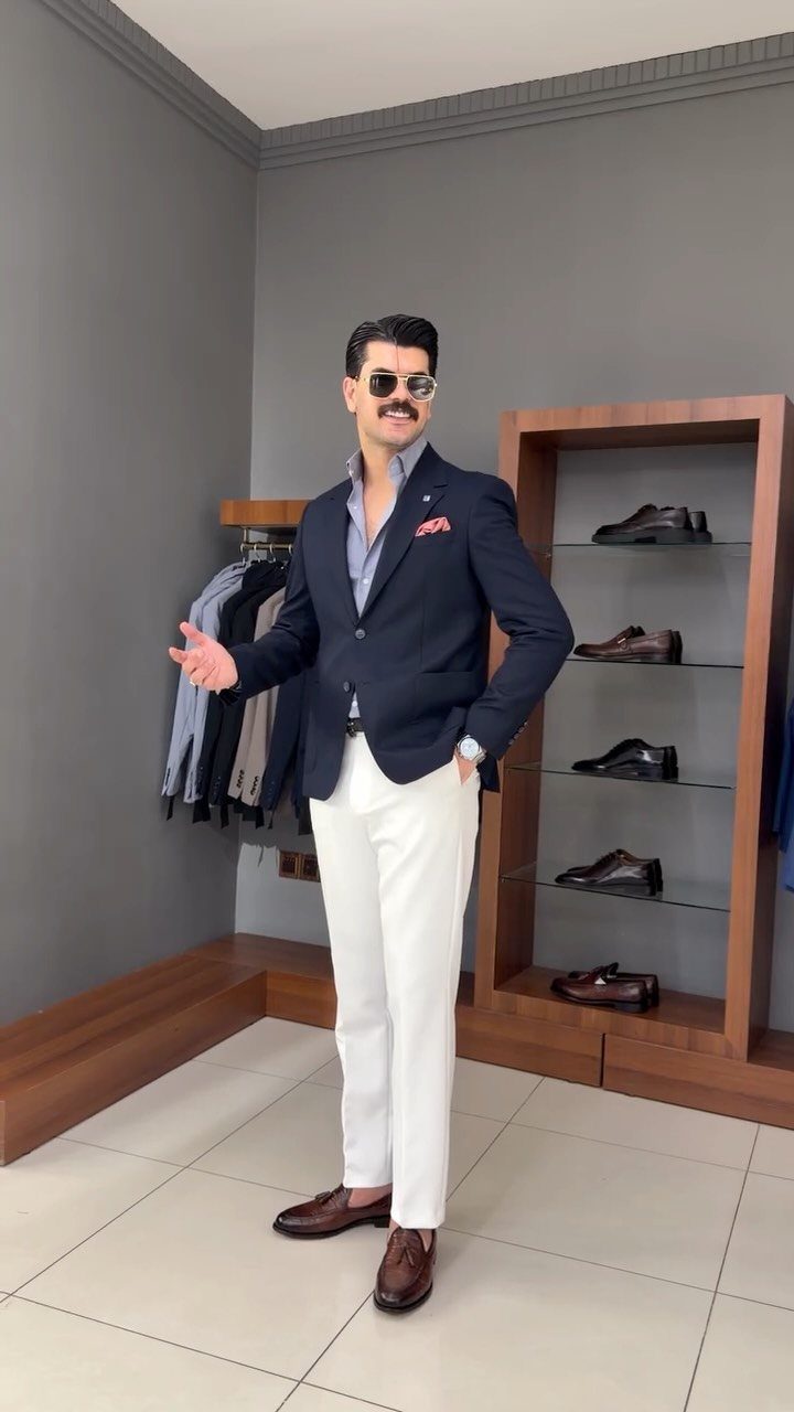 Man in a navy blazer, light blue shirt, and white trousers posing in a clothing store.