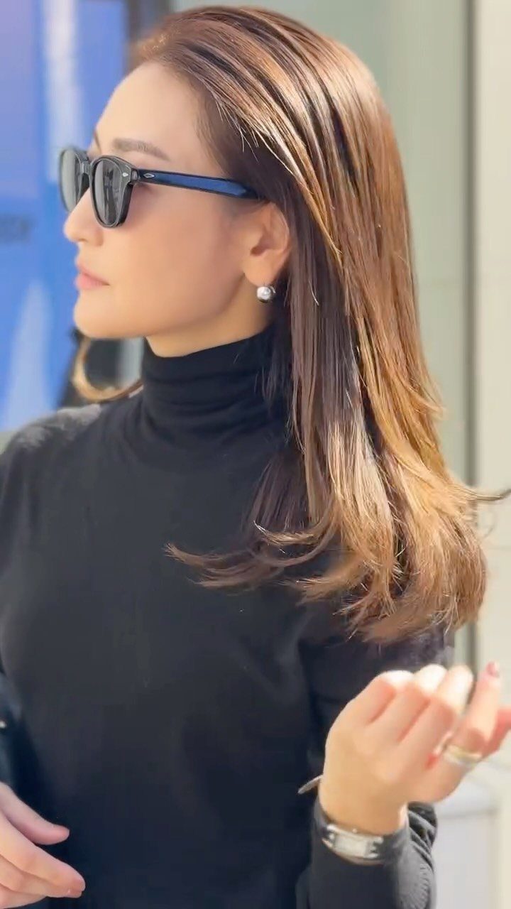 A woman in a black turtleneck and sunglasses wearing pearl stud earrings and a silver ring.