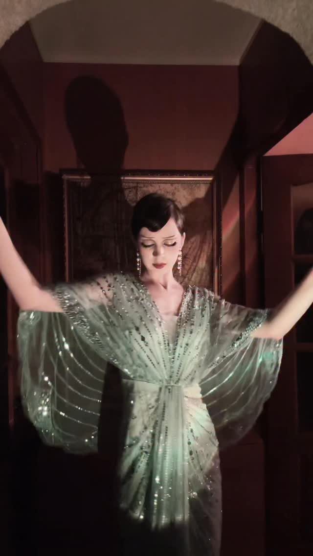 Woman in a shimmering green sequined gown posing in a dimly lit, dramatic room.