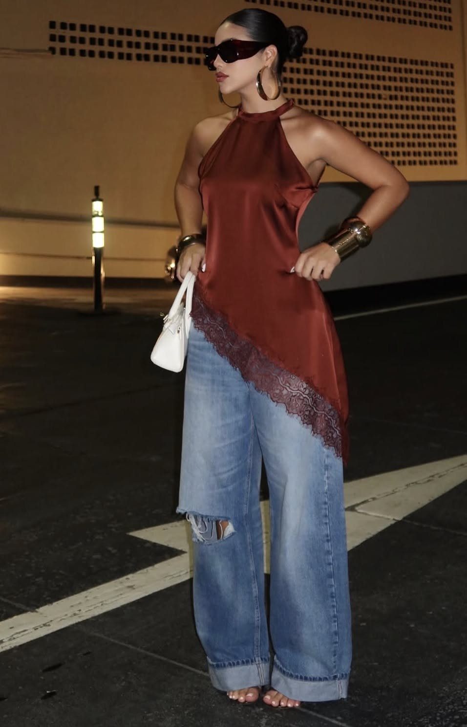 Woman in a red silk halter top and wide-leg denim jeans standing on a street at night.