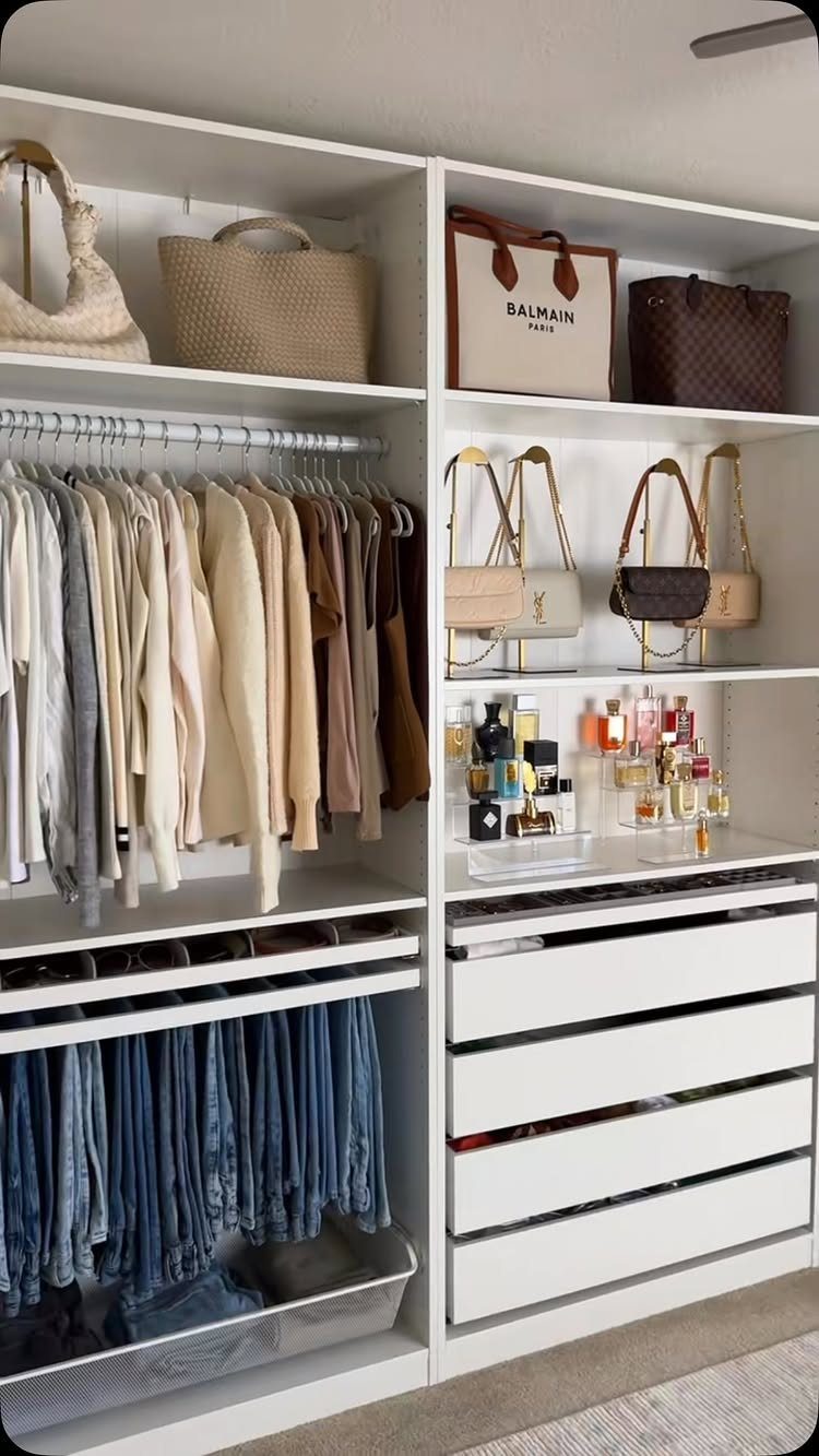 A white organized closet with neutral clothing, designer handbags, perfumes, and white drawers.