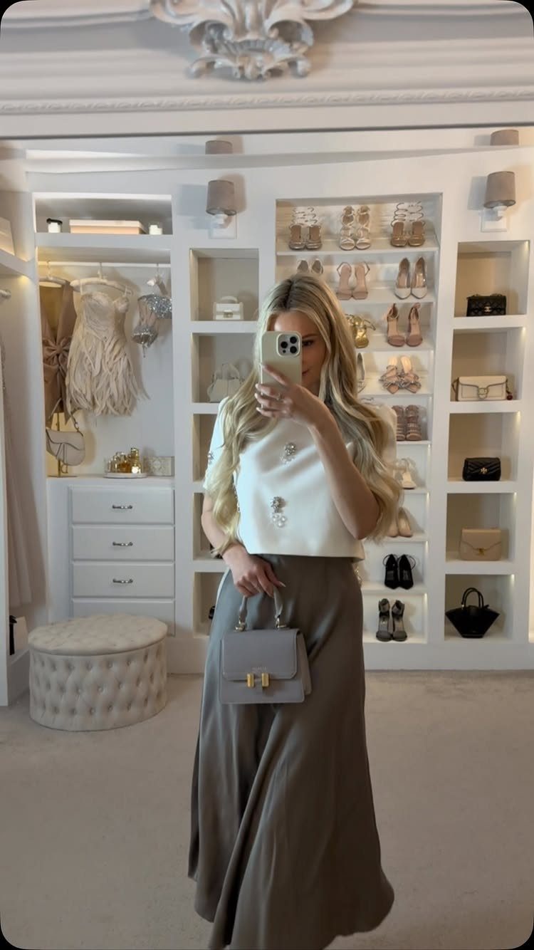 Woman in a white top and long grey skirt posing in a luxury walk-in closet.
